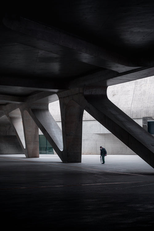 Person walking under a modern architectural structure with large concrete beams - primary